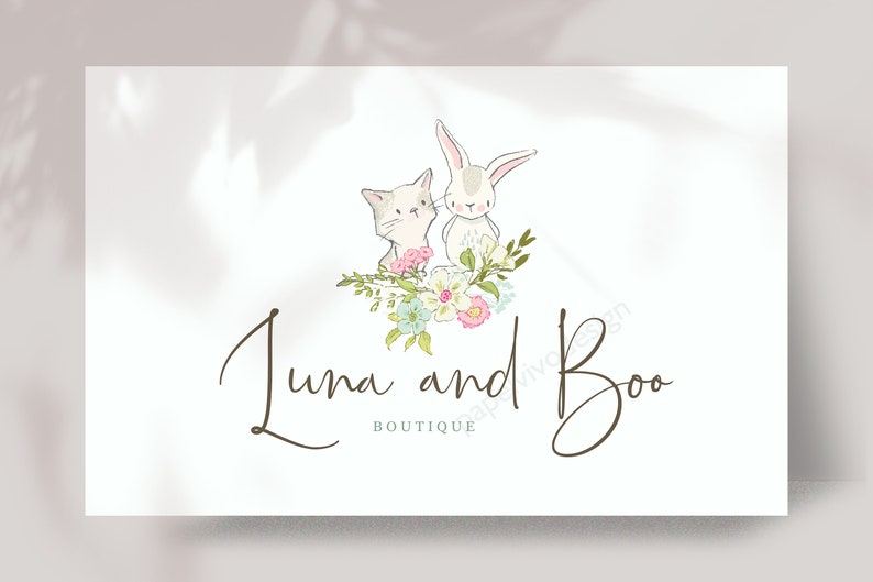 May include: A white cat and a white rabbit with pink noses are sitting in a bouquet of pink, white, and blue flowers. The text "Luna and Boo Boutique" is written in brown cursive script below the animals.