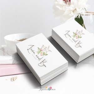 May include: Stack of white business cards with a logo featuring two cartoon bunnies with pink flowers and the text "Luna and Boo Boutique".