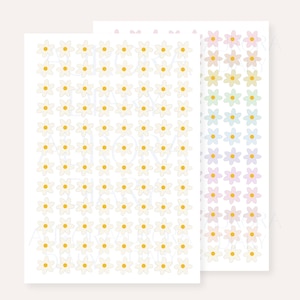 Pode incluir: Duas folhas retangulares de adesivos com fileiras de pequenas flores brancas de cinco pétalas com centros amarelos. A folha à direita exibe flores em um gradiente de cores pastéis, incluindo rosa, amarelo, verde, azul e roxo. Texto Aurora Diary.