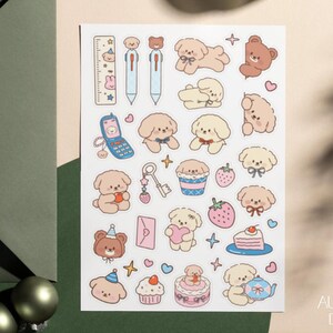 Peut inclure: Une planche d'autocollants pr&eacute;sentant diverses illustrations, dont des chiots brun clair et cr&egrave;me, un ours brun, un t&eacute;l&eacute;phone &agrave; clapet bleu, une cl&eacute;, des fraises, une part de g&acirc;teau, un cupcake, une th&eacute;i&egrave;re, une r&egrave;gle et des enveloppes roses.