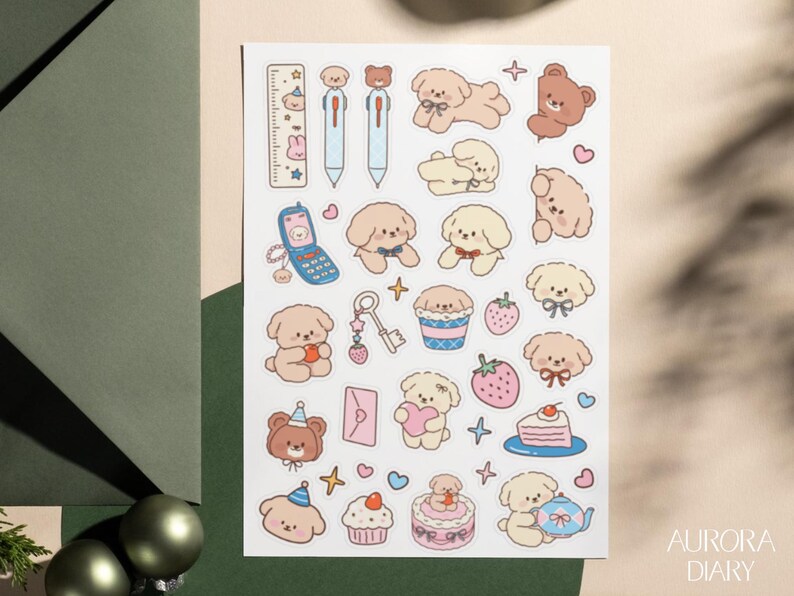 Peut inclure: Une planche d'autocollants pr&eacute;sentant diverses illustrations, dont des chiots brun clair et cr&egrave;me, un ours brun, un t&eacute;l&eacute;phone &agrave; clapet bleu, une cl&eacute;, des fraises, une part de g&acirc;teau, un cupcake, une th&eacute;i&egrave;re, une r&egrave;gle et des enveloppes roses.