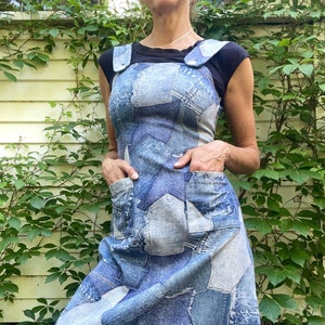 May include: A blue denim dress made from patchwork denim fabric. The dress has a sleeveless bodice and a straight skirt. The dress has two pockets on the front.