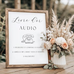 Peut inclure: Panneau en bois avec les mots "Livre d'Or AUDIO" et des instructions. Une illustration de téléphone vintage est en dessous du texte. Un arrangement floral avec des fleurs pêche et blanches se trouve à droite du panneau.