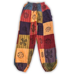 May include: Patchwork pants with a drawstring waist. The pants feature a variety of colorful squares in shades of orange, red, purple, and green. Each square is adorned with a black floral design. The pants have a relaxed fit and two pockets.