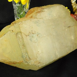 Pode incluir: Um grande cristal de quartzo transparente com um tom amarelo e uma superfície áspera e natural. O cristal tem uma ponta pontiaguda e uma base plana.