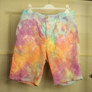 May include: Tie-dye shorts in shades of pink, orange, yellow, and blue. The shorts have a button fly and two pockets.