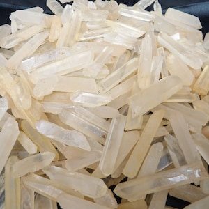 May include: A large pile of clear quartz crystal points. The points are various sizes and shapes, with some being longer and thinner than others. The crystals are all translucent and have a slight milky white color.