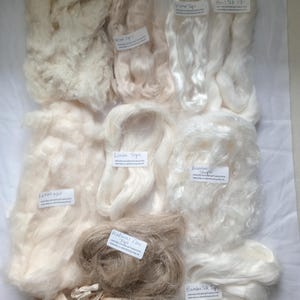 May include: A collection of various natural fiber samples, including linen, bamboo, and silk, in shades of white, cream, and tan. Each sample is labeled with its fiber type. The fibers are arranged on a white surface.