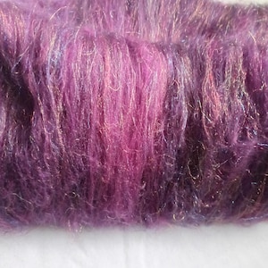 Könnte beinhalten: Ein Bündel aus flauschigem, tiefviolettem Garn mit einer Mischung aus violetten und magentafarbenen Fasern und eingewebten, dezenten Metallic-Fäden, das eine weiche, strukturierte Optik mit einem leichten Glanz auf der gesamten Oberfläche aufweist.
