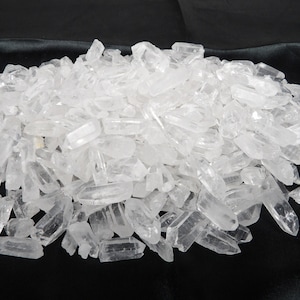 Puede incluir: Un montón grande de puntas de cristal de cuarzo transparente. Las puntas son de varios tamaños y formas, y todas están agrupadas en un fondo negro.