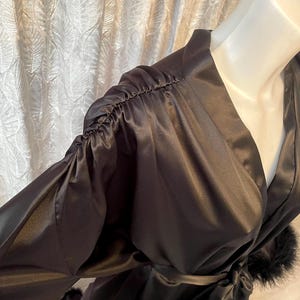 May include: A black satin robe with long sleeves and a wrap-around design. The sleeves are gathered at the shoulders, and the robe is trimmed with black feathers. A matching belt is tied at the waist.