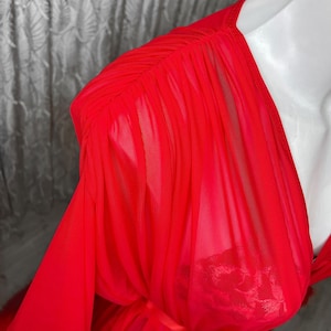 May include: A red sheer robe with a ruffled neckline and long sleeves. The robe is made of a lightweight, flowing fabric and has a tie at the waist.