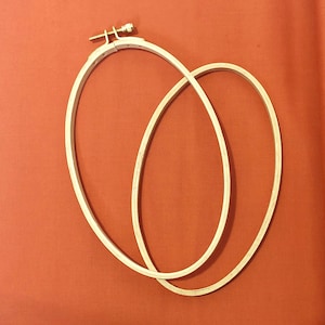 May include: Two wooden embroidery hoops, one slightly larger than the other, are nested together. The hoops are made of natural wood and have a smooth finish. The hoops are used for stretching fabric for embroidery.