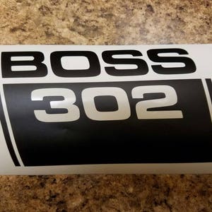 May include: White vinyl decal with black lettering that reads "BOSS 302".