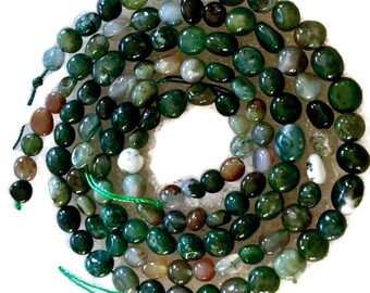 Pode incluir: Um colar de contas de pedras preciosas polidas em tons de verde, castanho e branco. As contas são ovais e de formato irregular, enfiadas com fio verde. As contas variam em tamanho e cor, criando um visual natural e orgânico.