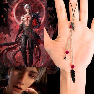 Puede incluir: Un collar con colgante de pluma negra con cadena plateada y cuentas rojas y negras. El collar se muestra en una mano sobre un fondo negro. La imagen también incluye una ilustración digital de un personaje masculino.