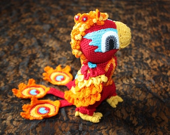 May include: A crocheted stuffed toy bird with a red body, yellow and orange feathers, and blue and white eyes. The bird has a crown of orange and yellow crocheted feathers.