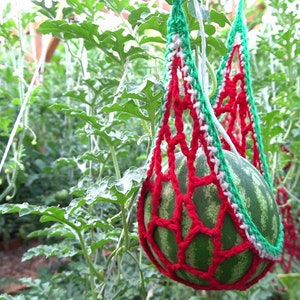 Puede incluir: Una sandía verde colgando en una red de crochet roja, blanca y verde en un invernadero.