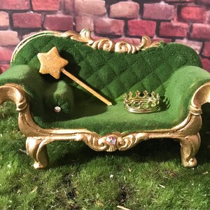 May include: A miniature green velvet chaise lounge with gold accents, featuring a gold crown and a gold star-shaped wand on top.