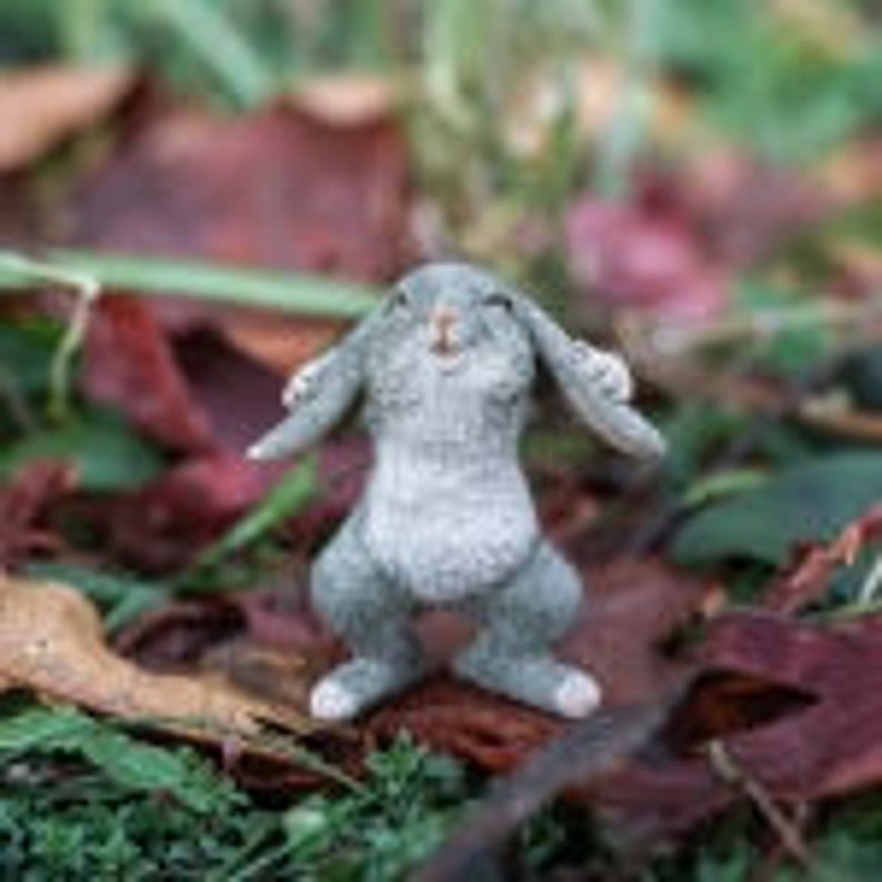 May include: A small gray rabbit figurine with a happy expression, standing on its hind legs with its front paws raised. The figurine is made of a textured material and has a realistic appearance.