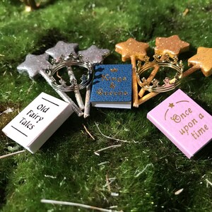 May include: A set of miniature fairy tale themed books and wands. The books are titled "Old Fairy Tales", "Kings & Queens", and "Once Upon a Time". The wands are silver and gold with star-shaped tops.