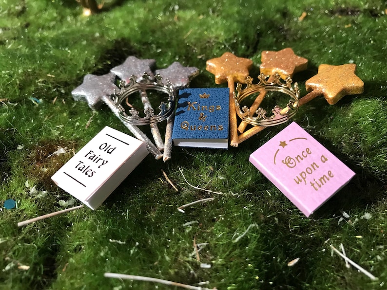 May include: A set of miniature fairy tale themed books and wands. The books are titled "Old Fairy Tales", "Kings & Queens", and "Once Upon a Time". The wands are silver and gold with star-shaped tops.