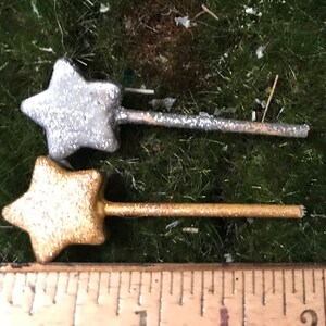 May include: Two miniature star-shaped wands, one silver and one gold, with glitter accents. The wands are approximately 2 inches long and are shown next to a ruler.
