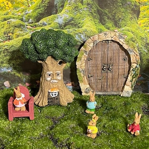 Peut inclure: Une scène de jardin féerique fantaisiste avec un arbre au visage humain, une porte en pierre et plusieurs petits lapins. Les lapins portent des pulls et sont assis sur une chaise rouge, créant un cadre forestier charmant.