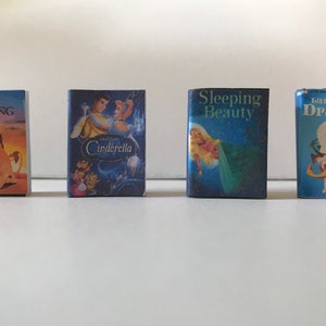 May include: Four miniature Disney storybook covers featuring The Lion King, Cinderella, Sleeping Beauty, and Little Mother Dragons. The covers are blue with colorful illustrations of the characters.