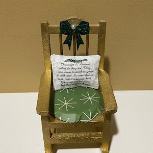 May include: A miniature rocking chair with a green bow and a pillow with the text "Christmas in Heaven, what do they do? They came down to earth to spend it with you. So save them a seat, just one empty chair. You may not see them, but they will be there."