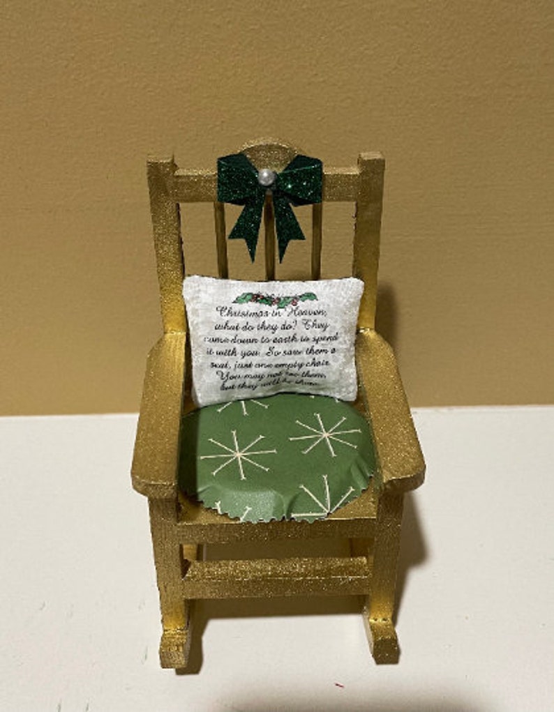 May include: A miniature rocking chair with a green bow and a pillow with the text "Christmas in Heaven, what do they do? They came down to earth to spend it with you. So save them a seat, just one empty chair. You may not see them, but they will be there."