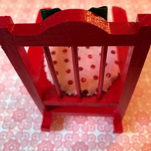 May include: A red wooden rocking chair with a white and red polka dot cushion. The chair has a high back and a simple design.