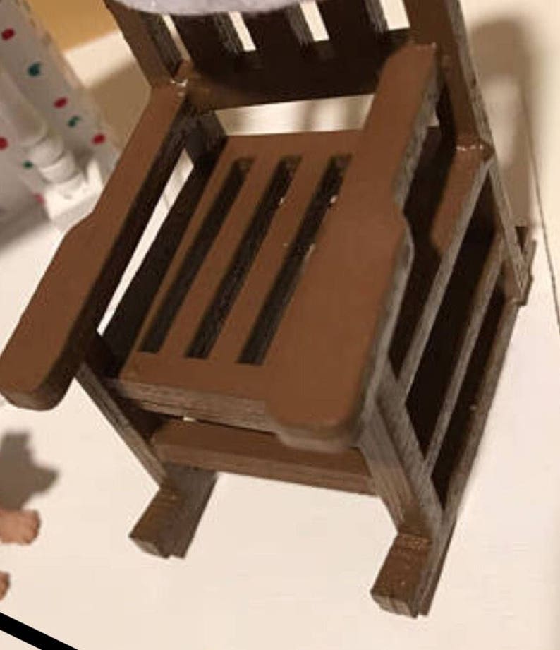 Op de afbeelding: Een bruine houten schommelstoel met een latten zitting en rugleuning. De stoel is gemaakt van onbehandeld hout en heeft een rustieke uitstraling.