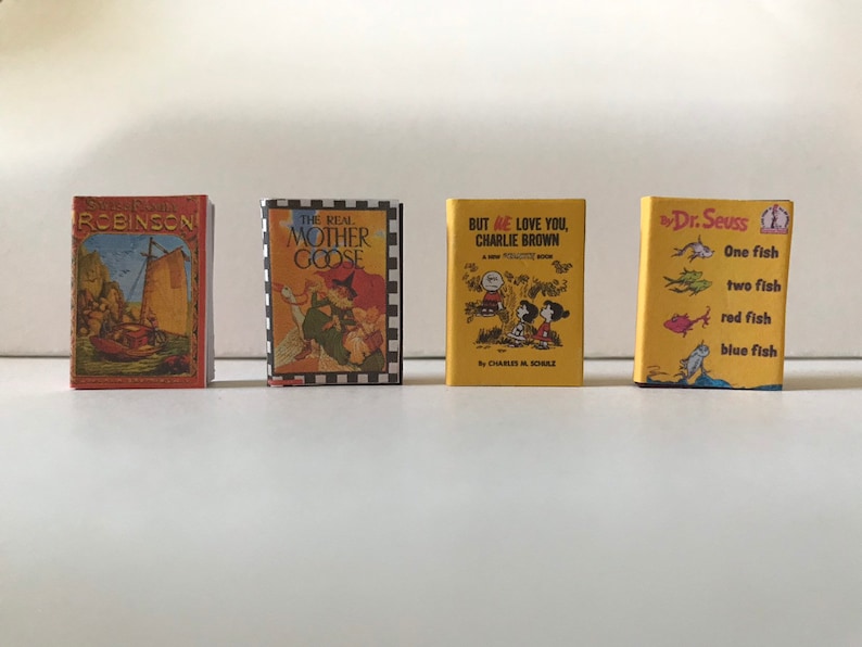 May include: Four miniature hardcover books with colorful covers. The titles are "Robinson", "The Real Mother Goose", "But We Love You, Charlie Brown", and "One Fish, Two Fish, Red Fish, Blue Fish" by Dr. Seuss.