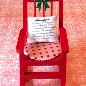 May include: A red rocking chair with a white cushion featuring the text "Christmas in Heaven, what do they do? They come down to earth to spend time with you. So save them a seat, just one empty chair. You may not see them, but they will be there." The chair has a pink and white polka dot cushion and a green glitter bow on the back.