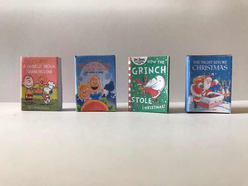May include: Four miniature hardcover books with colorful covers. The books are titled "A Charlie Brown Thanksgiving", "It's the Great Pumpkin, Charlie Brown", "How the Grinch Stole Christmas!" and "The Night Before Christmas".