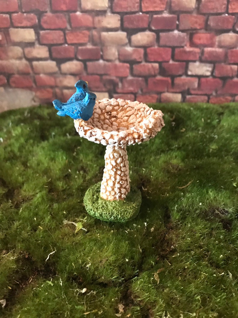K&ouml;nnte beinhalten: Ein Miniatur-Vogelbad mit wei&szlig;er, strukturierter Oberfl&auml;che und gr&uuml;nem Sockel. Zwei blaue V&ouml;gel sitzen auf dem Rand des Bades.