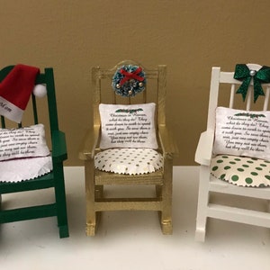 May include: Three miniature rocking chairs decorated for Christmas. The chairs are painted green, gold, and white. Each chair has a pillow with a Christmas poem printed on it. The green chair has a Santa hat on the back, the gold chair has a wreath with red berries, and the white chair has a green bow.