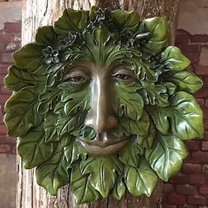 May include: A green, leafy face sculpture with a smiling expression. The face is made of a textured material and has a realistic appearance.