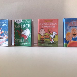 May include: Four miniature hardcover books with colorful covers. The books are titled "The Night Before Christmas", "How the Grinch Stole Christmas!" by Dr. Seuss, "A Charlie Brown Thanksgiving" by Charles M. Schulz, and "It's the Great Pumpkin, Charlie Brown" by Charles M. Schulz.