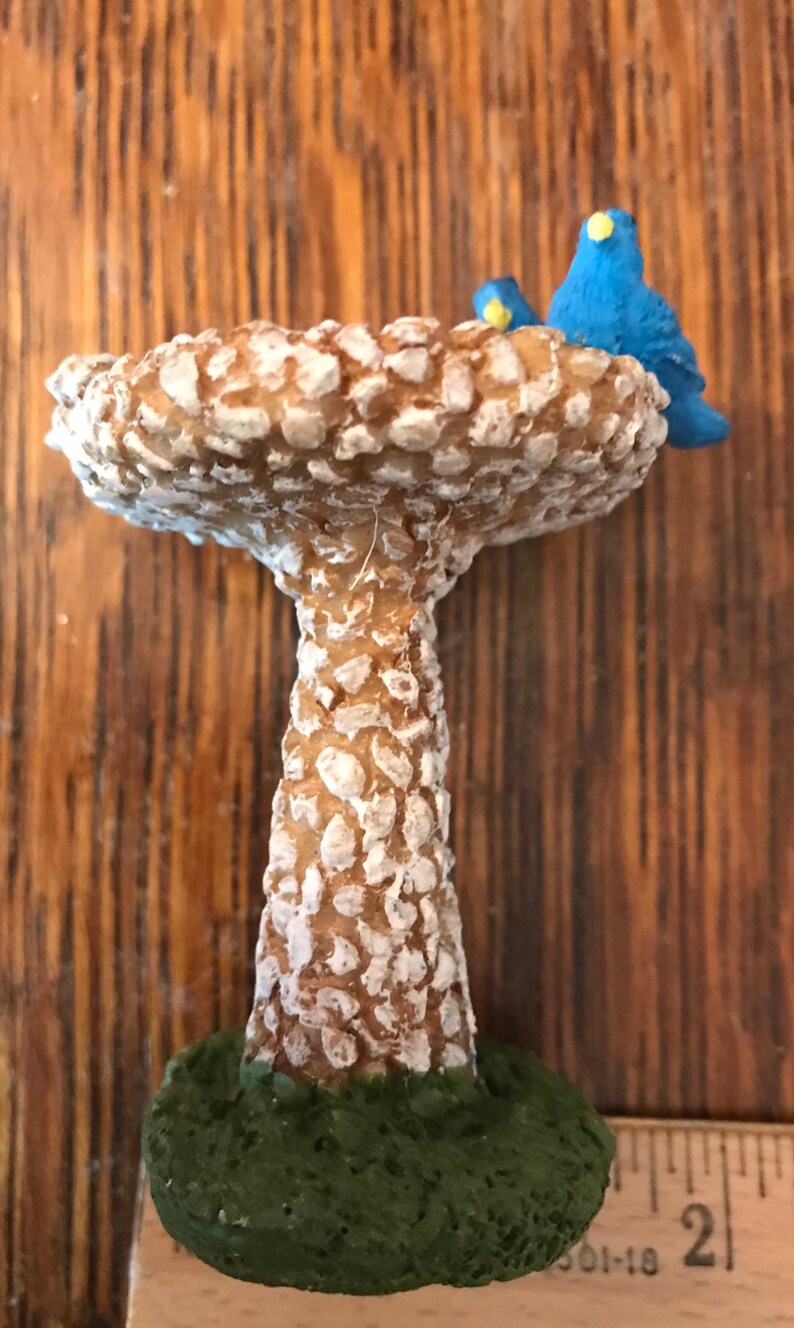 K&ouml;nnte beinhalten: Ein Miniatur-Vogelbad aus brauner und wei&szlig;er, gesprenkelter Keramik. Das Bad ist in Form eines Pilzes mit einer breiten, flachen Oberseite und einem hohen, schlanken Stiel. Zwei kleine blaue V&ouml;gel sitzen auf dem Rand des Bades.