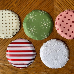 May include: Five round paper cupcake liners with scalloped edges. The liners are decorated with different festive patterns: gold and white diamonds, green with white snowflakes, pink with red polka dots, red and white stripes, and white with embossed snowflakes.