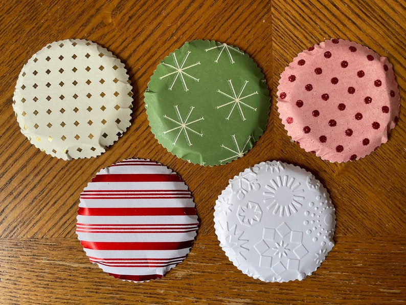 May include: Five round paper cupcake liners with scalloped edges. The liners are decorated with different festive patterns: gold and white diamonds, green with white snowflakes, pink with red polka dots, red and white stripes, and white with embossed snowflakes.