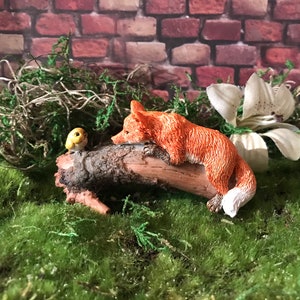 Sweet fairy garden red Fox Laying on a log making friends with a little yellow bird