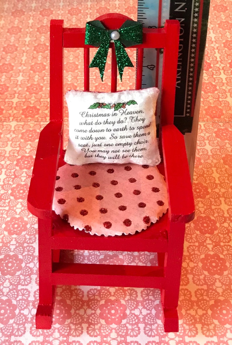 May include: A red rocking chair with a white cushion featuring the text "Christmas in Heaven, what do they do? They come down to earth to spend it with you. So save them a seat, just one empty chair. You may not see them, but they will be there." The chair has a pink and red polka dot cushion.