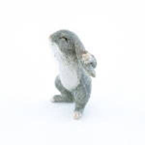 May include: A small, gray and white, plush toy rabbit with a sitting pose. The rabbit has a white belly and a pink nose.
