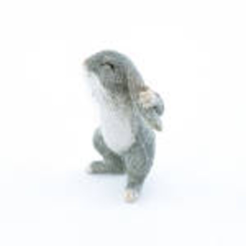 May include: A small, gray and white, plush toy rabbit with a sitting pose. The rabbit has a white belly and a pink nose.