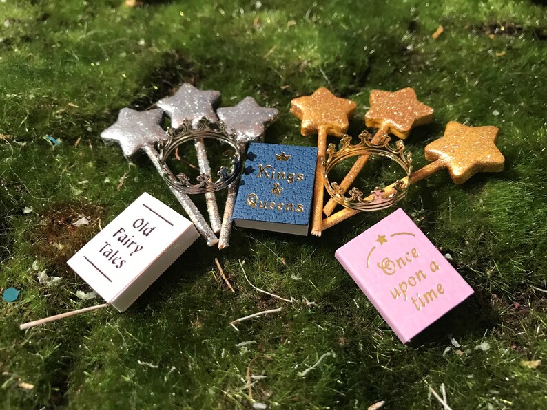 May include: A set of miniature fairy tale themed items, including three gold star wands, two silver star wands, a gold crown, and four small books with titles "Old Fairy Tales", "Kings & Queens", "Once Upon a Time", and a fourth book with an illegible title.