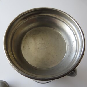 May include: A vintage pewter bowl with a handle. The bowl has a wide rim and a slightly textured surface. The interior is smooth and shows signs of age. The bowl is likely used for serving or display.
