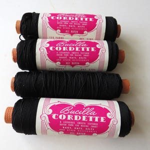 May include: Four spools of black Bucilla Cordette rayon yarn, each featuring a pink label with white text stating Bucilla Cordette, a luxurious smooth textured rayon yarn for making smart bags, hats, belts and other accessories, all rayon, 125 yards.